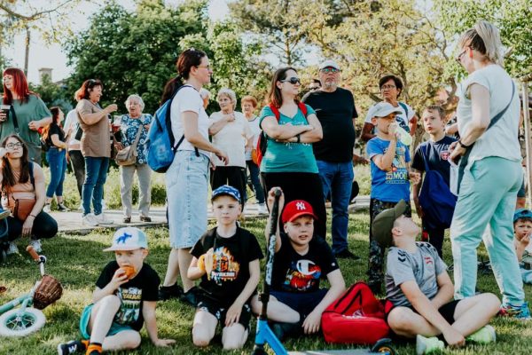 A diverse group of families and children enjoying an outdoor event on a sunny day in a park setting.
